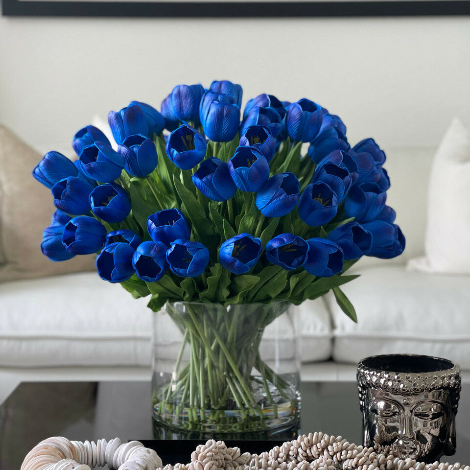 Arrangement de tulipes bleues dans un grand vase cylindrique.