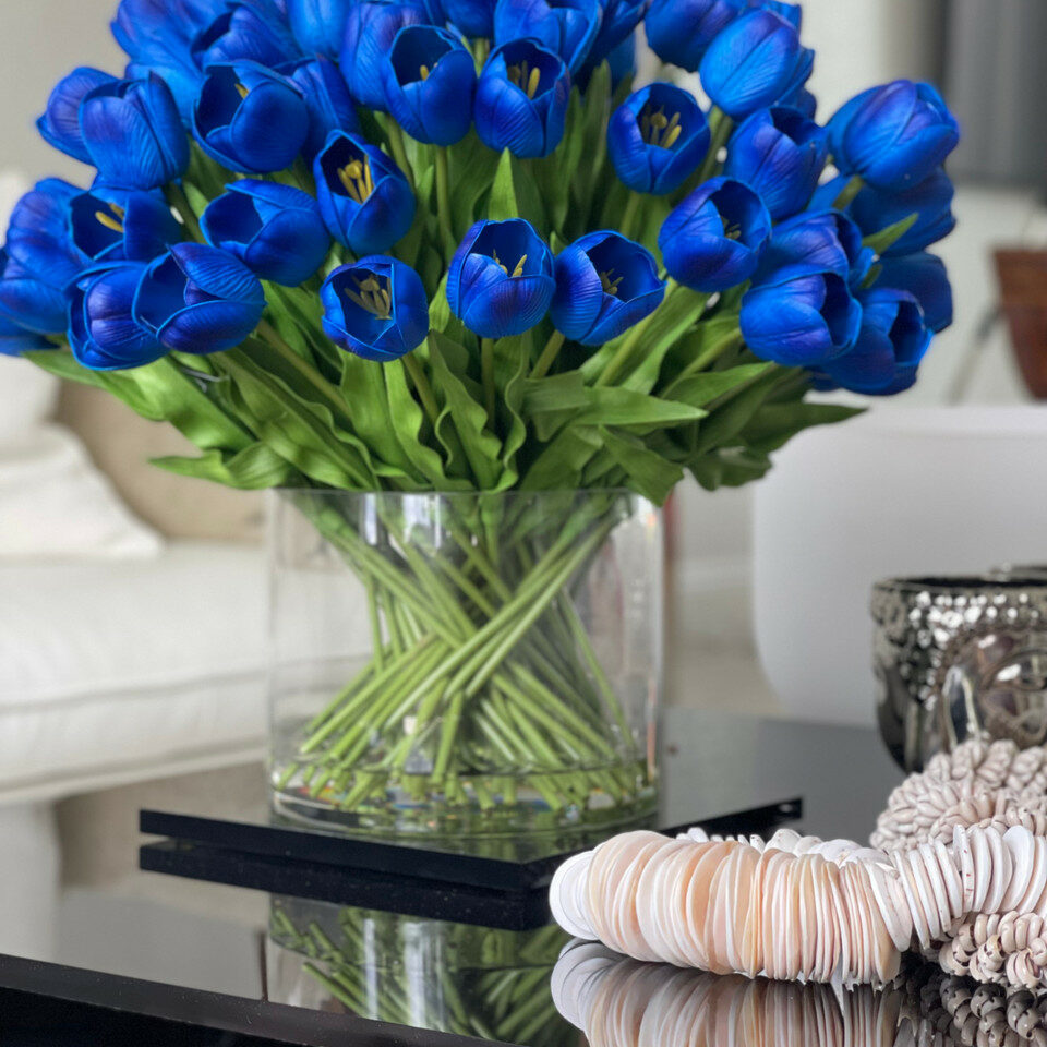 Arrangement de tulipes bleues dans un grand vase cylindrique.